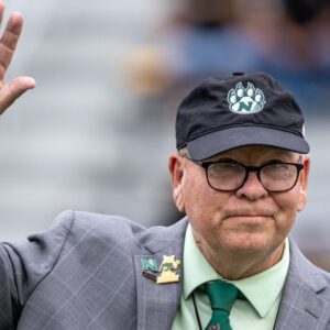 A man waving with glasses and a hat on