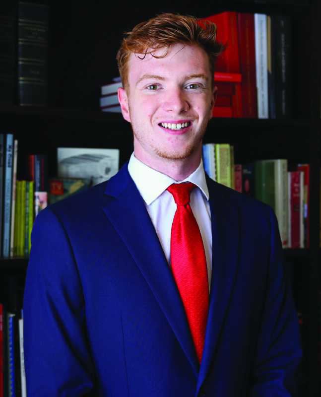 Photo of a man in a suit in front of a bookcase