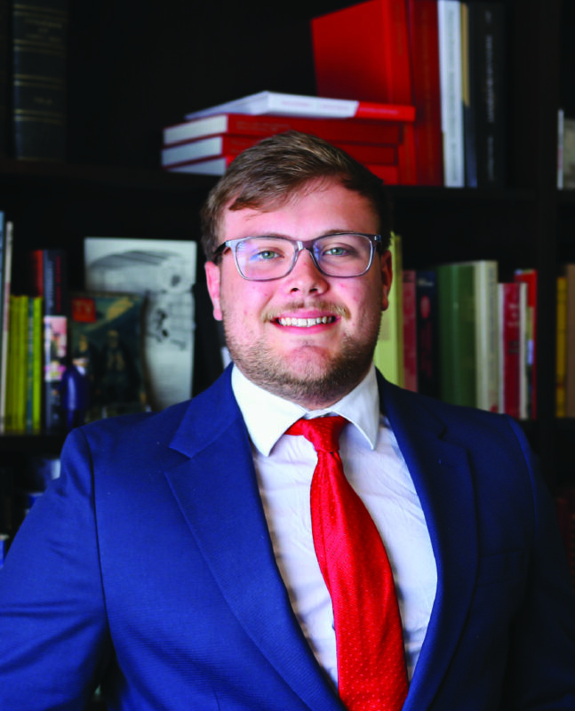 Photo of a man in a suit in front of a bookcase