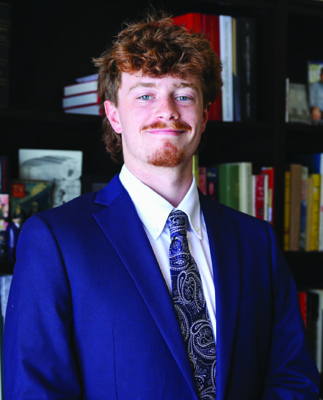 Photo of a man in a suit in front of a bookcase
