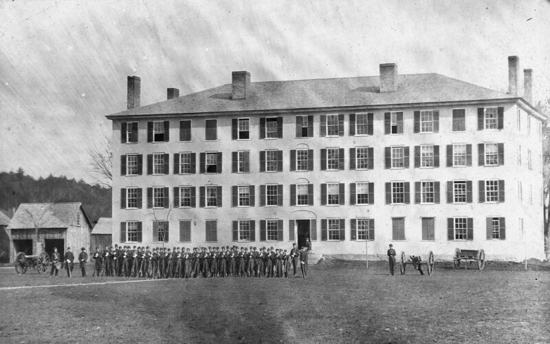 A black and white photo of men in front of an old style military building.