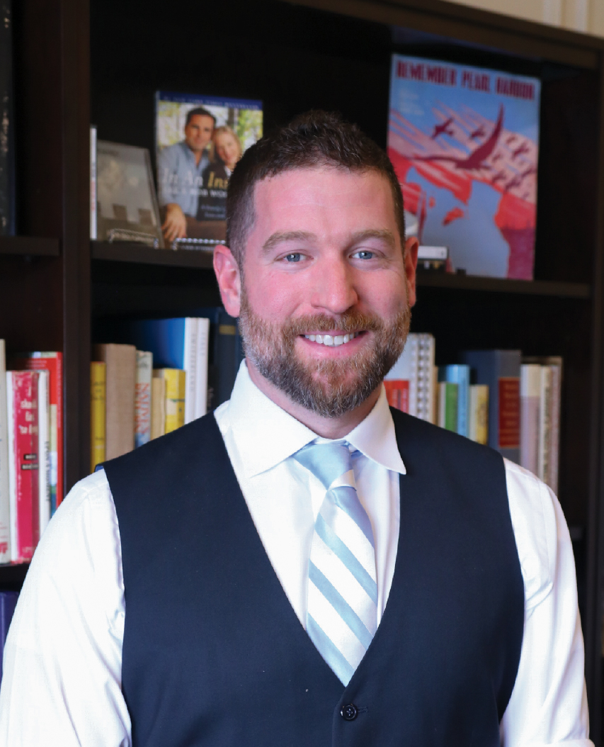 Photo of a man in a suit in front of a bookcase