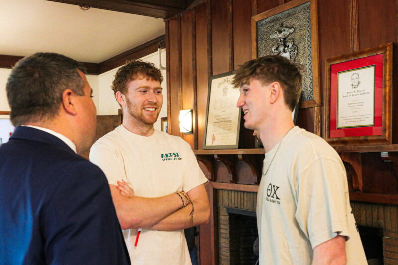 Two collegians in t-shirts laughing with a c-suite officer in a suit
