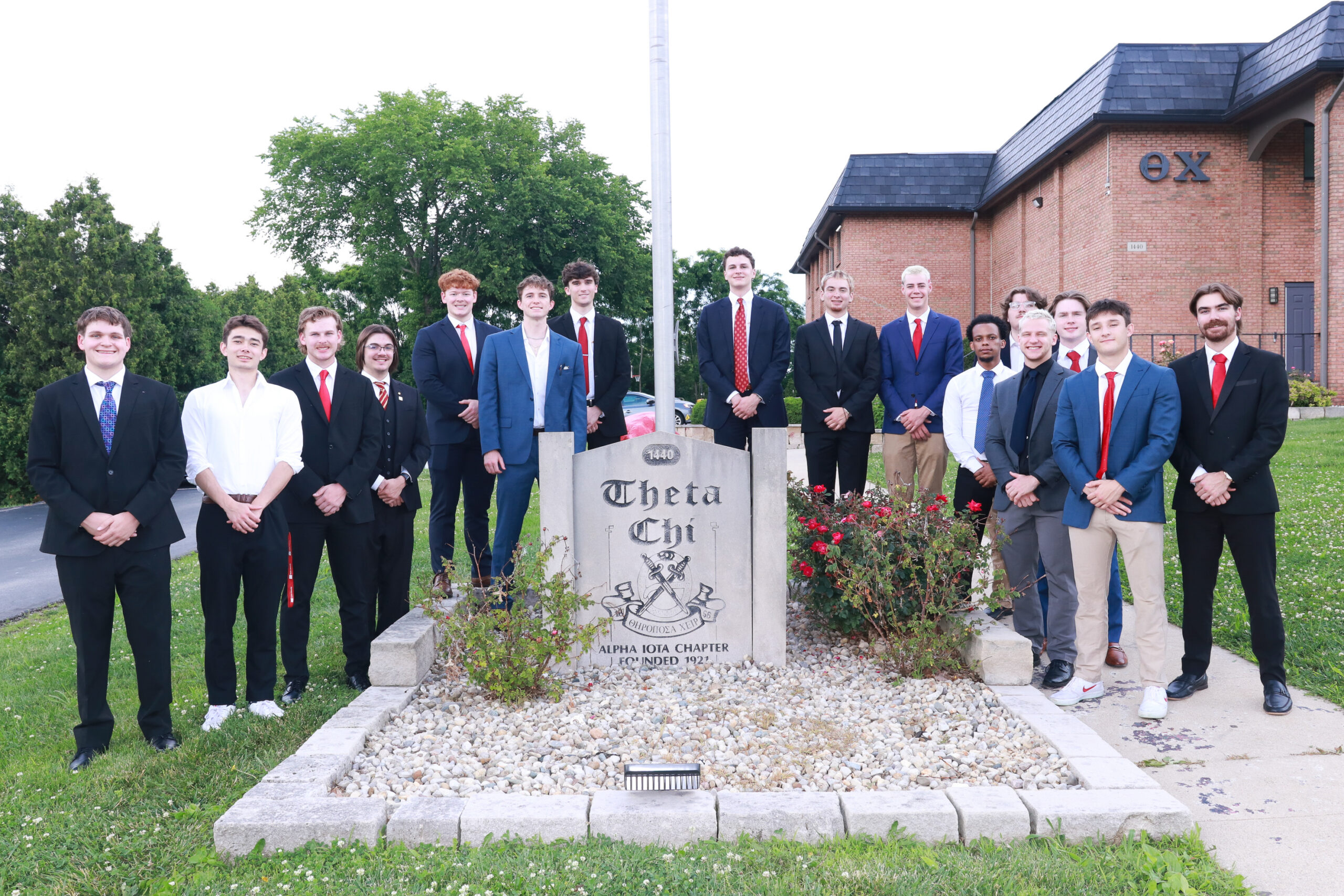 Brothers in suits standing around a flagpole and entrance sign
