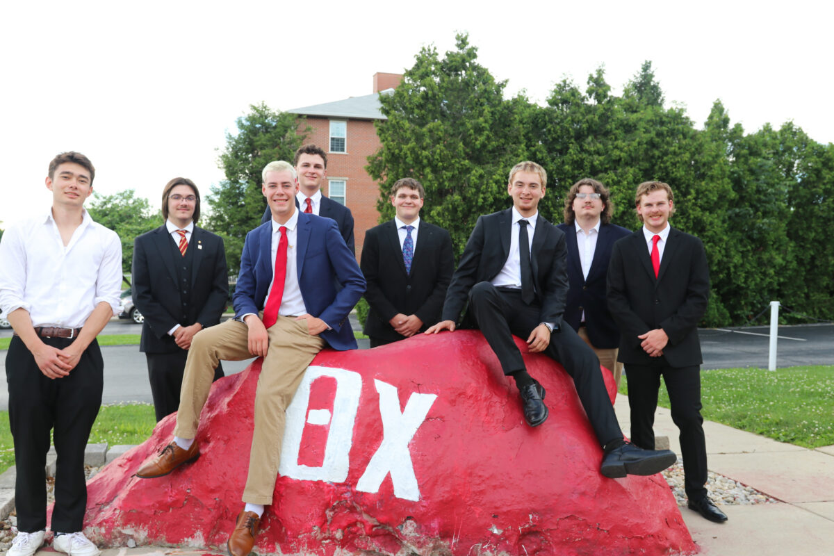 Brothers at Initiative Academy in suits by a decorative boulder