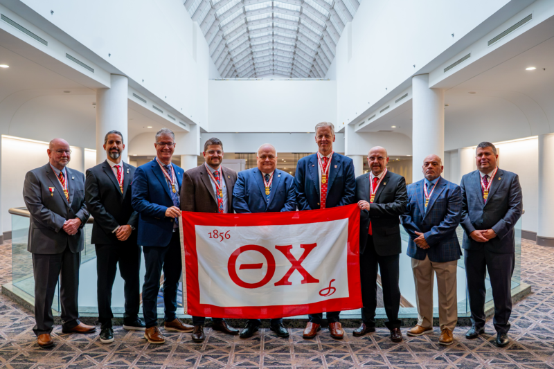 The Grand Chapter standing together with a Theta Chi Flag
